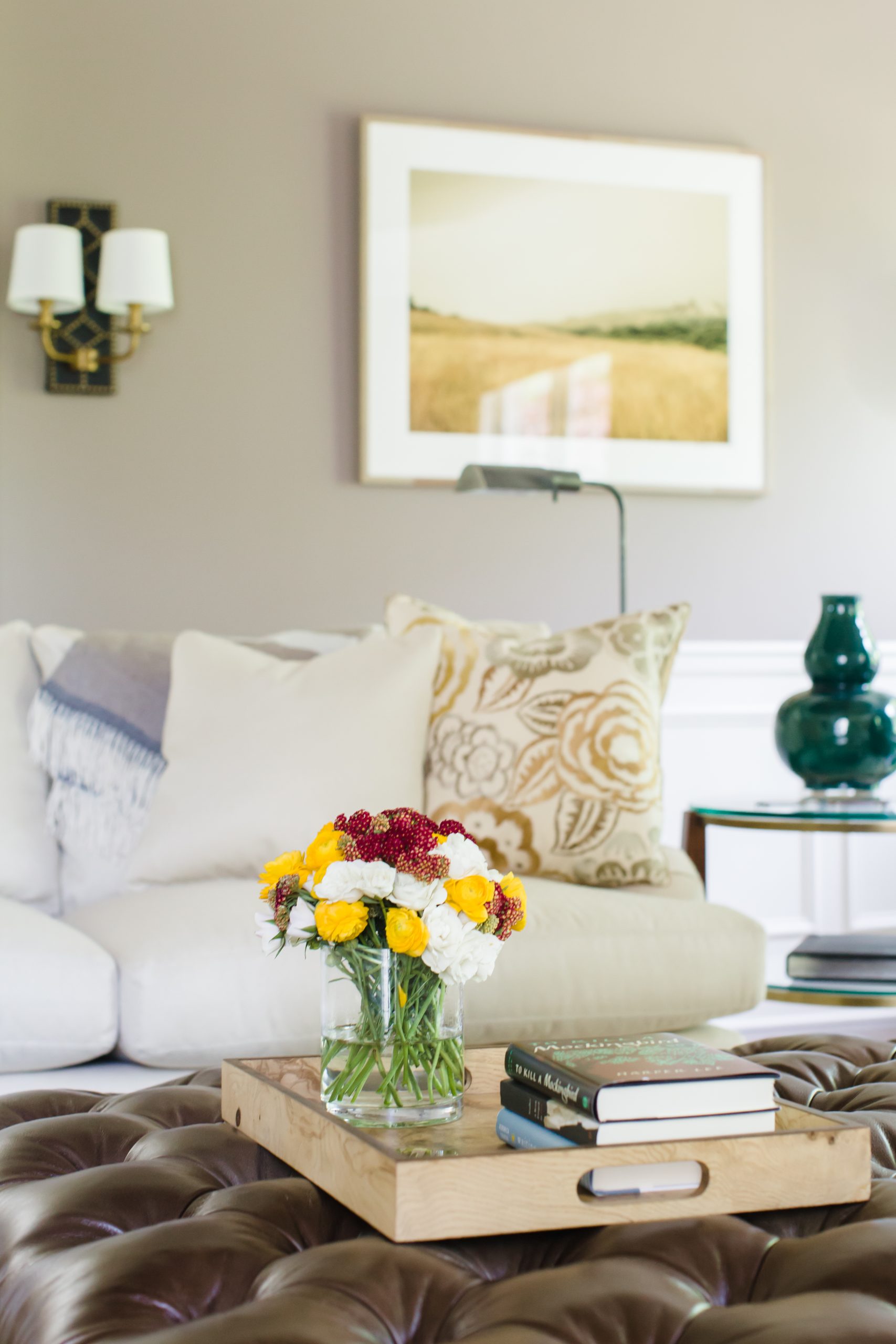 Transitional family room with grey wall color, beige furniture cushions, and a brown leather tufted ottoman with flower jar