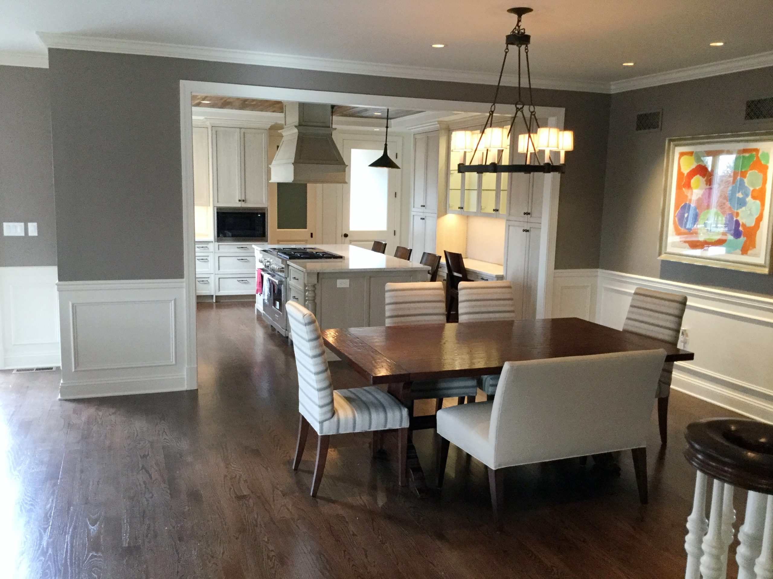 Transitional dining room with dark hardwood flooring and dining table, striped accented dining chairs, and light beige bench