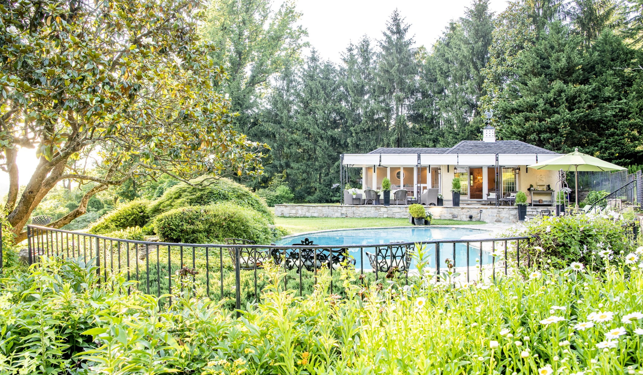 Luxury pool house custom designed for a home remodel with a large seating space and large metal pergola (Outside fence view)