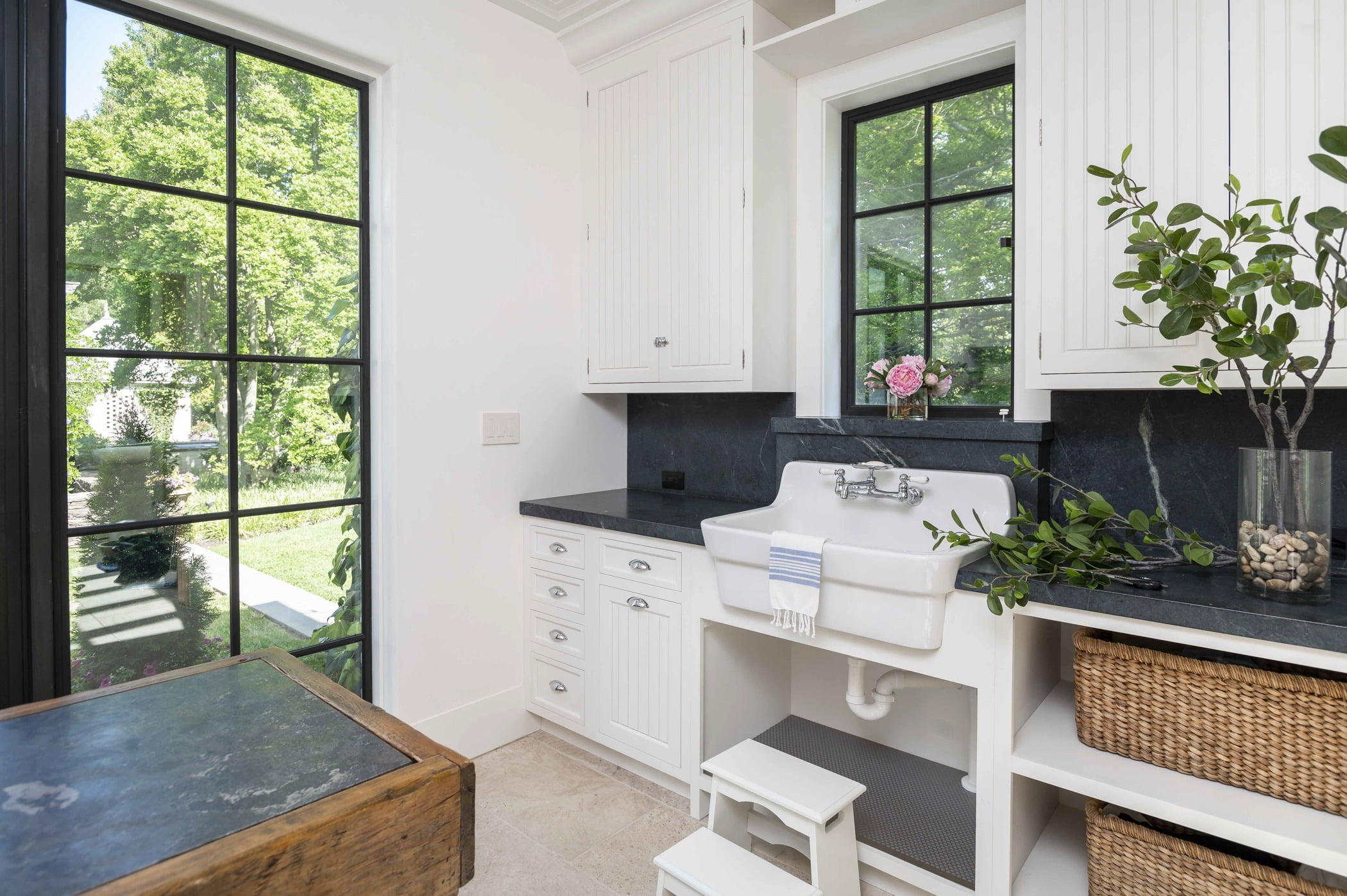 Coastal style washroom with white paneled cabinetry, dark granite countertops, and a dark metal window and door accent (Different angle)