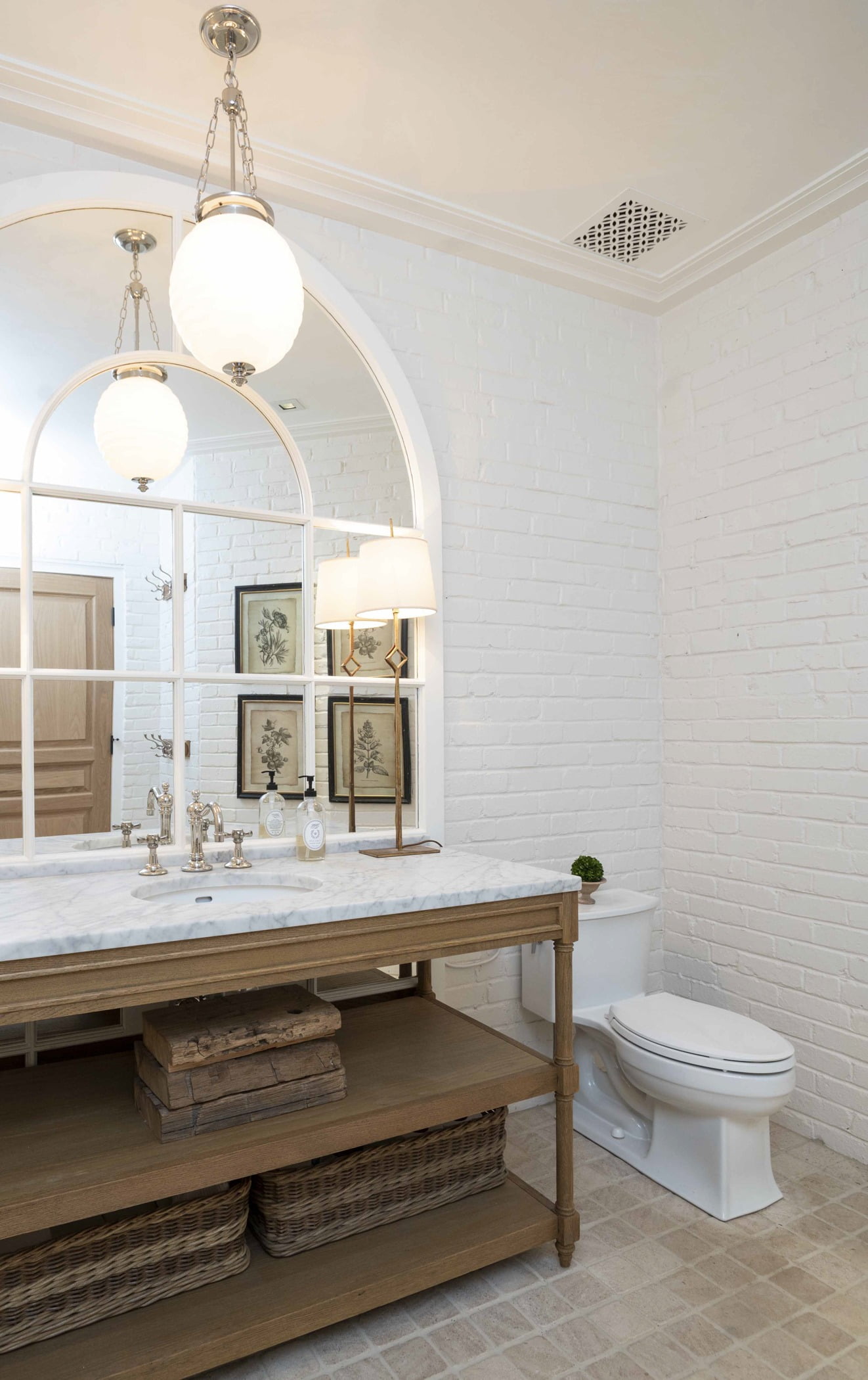 Traditional powder bathroom with wood cabinetry and marble countertops, beige square tile flooring, and painted white brick walls