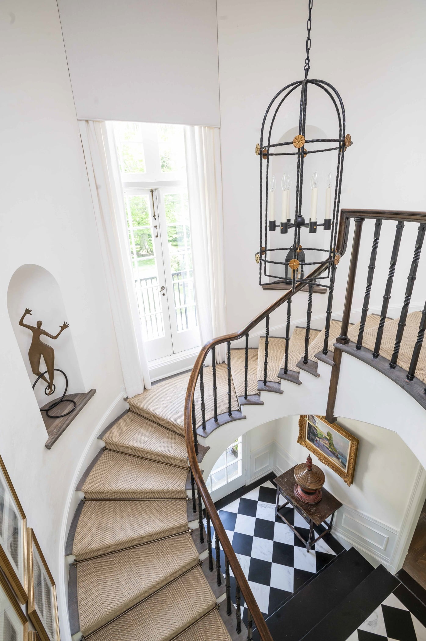 Grand staircase with wood railing, light carpeting and white wall color near a large window