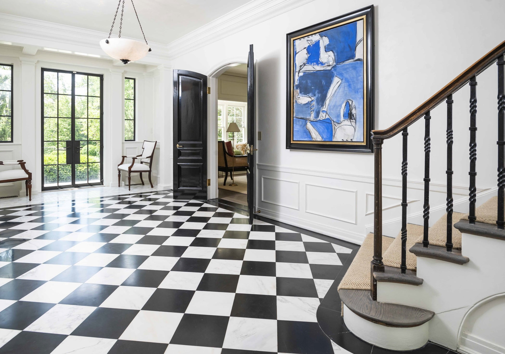 Traditional foyer with black and white checkered tile flooring, white wall color with molding, and black accent doors, frames, and balusters