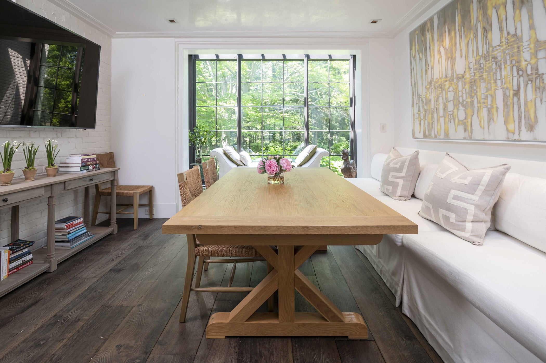 Transitional dining area with light hardwood dining table and two wicker chairs, wall-to-wall bench with throw pillows, and dark hardwood flooring