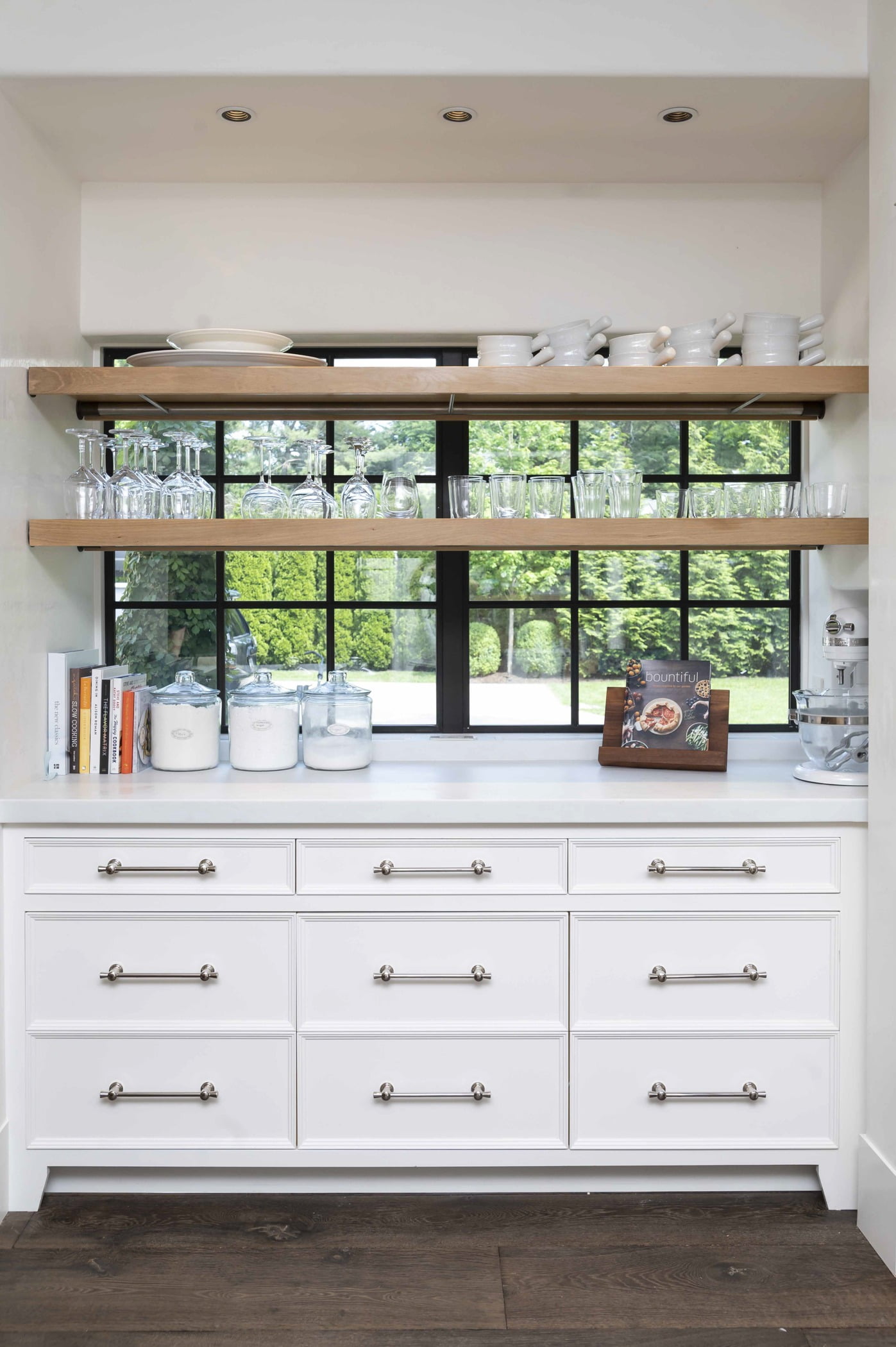 Custom white cabinetry with marble countertops and dark hardwood flooring and wood shelving and black window frames