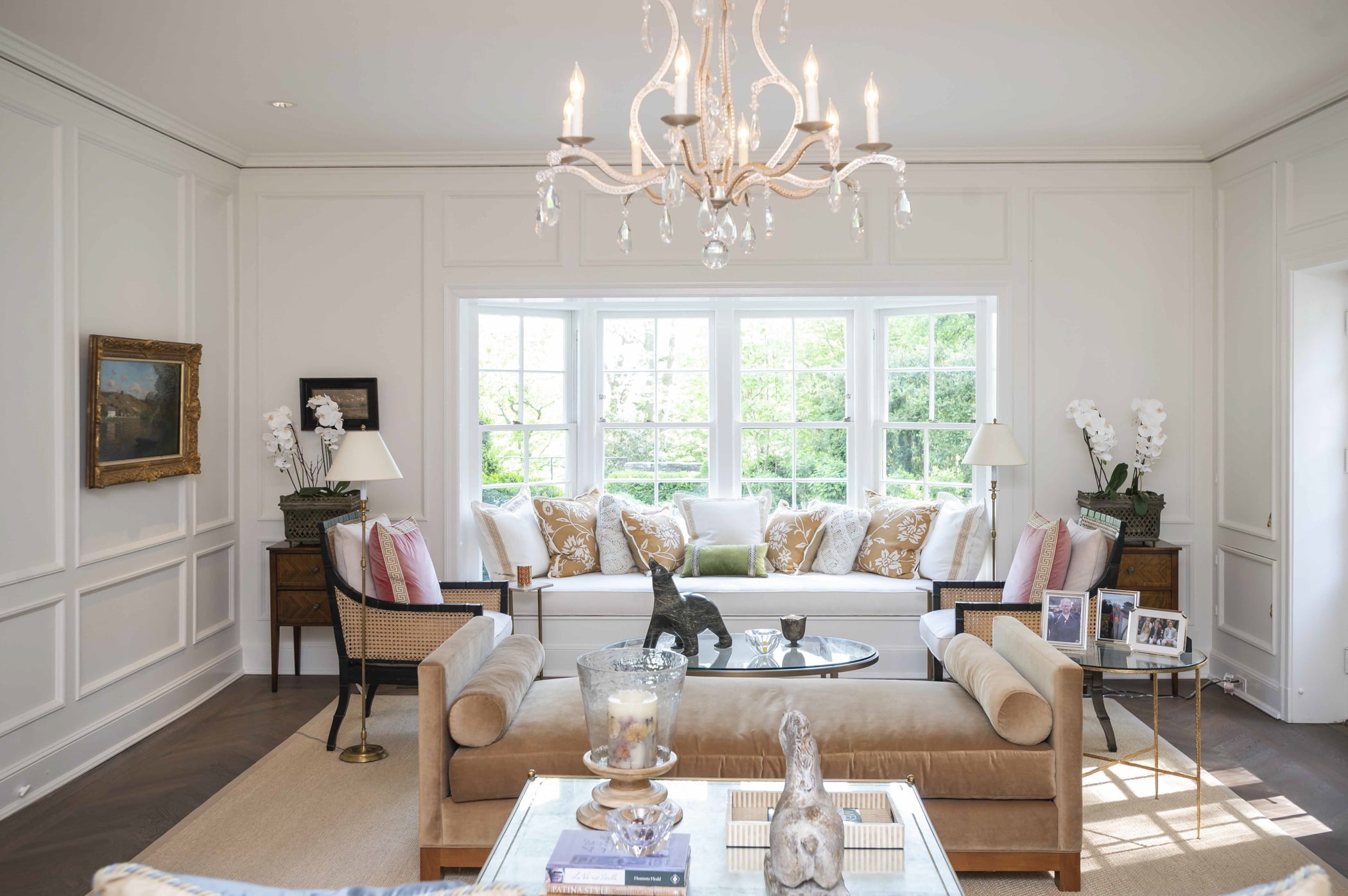 Transitional living room with dark hardwood chevron flooring, ornate chandelier, white walls with molding, and lightly colored furniture