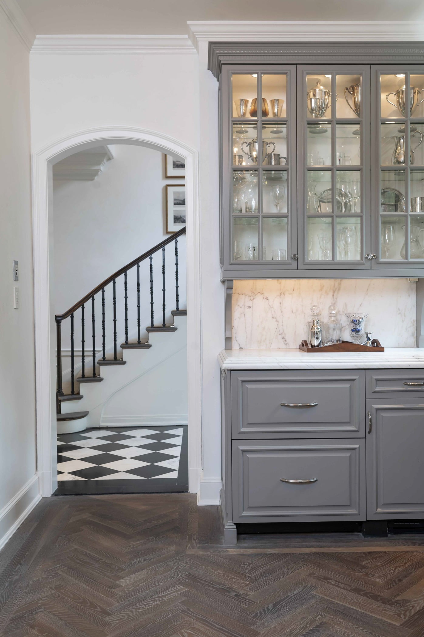 Traditional kitchen area with custom light grey cabinetry, marble countertops, and dark chevron hardwood flooring (Doorway view)