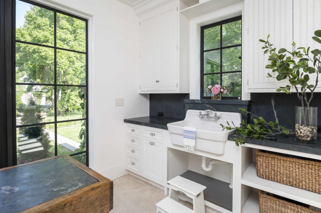 European farmhouse style washroom with white paneled cabinetry, dark granite countertops, and a dark metal window and door accent