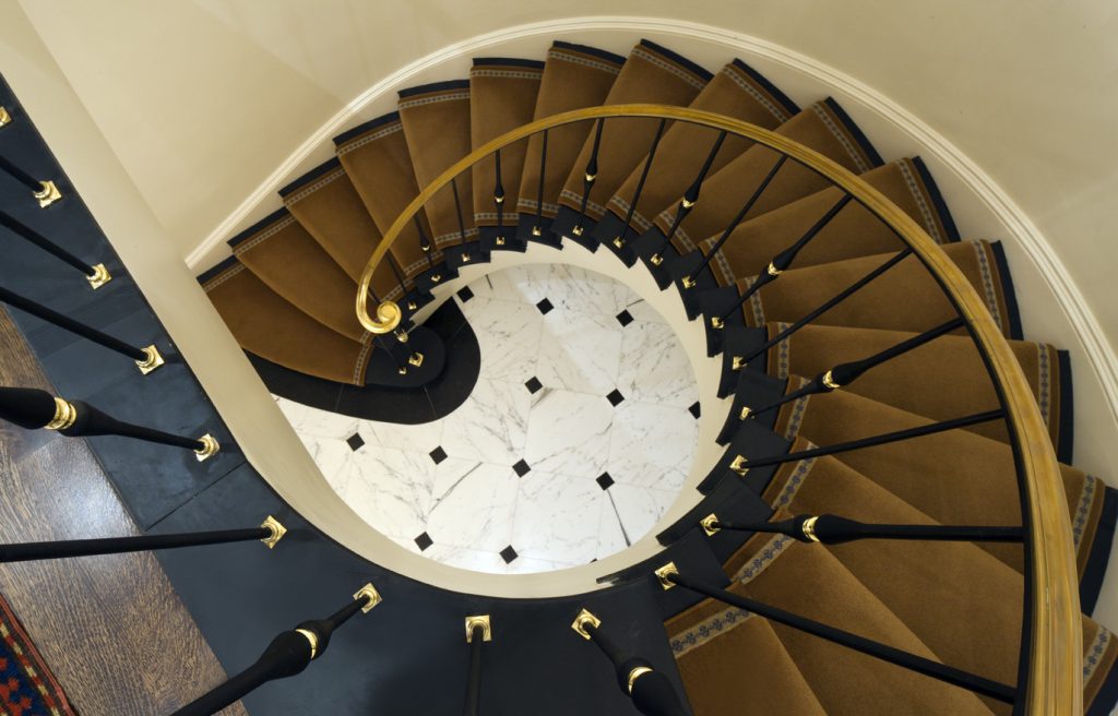 Victorian style metal spiral staircase with gold trim, gold carpet, and granite tile flooring