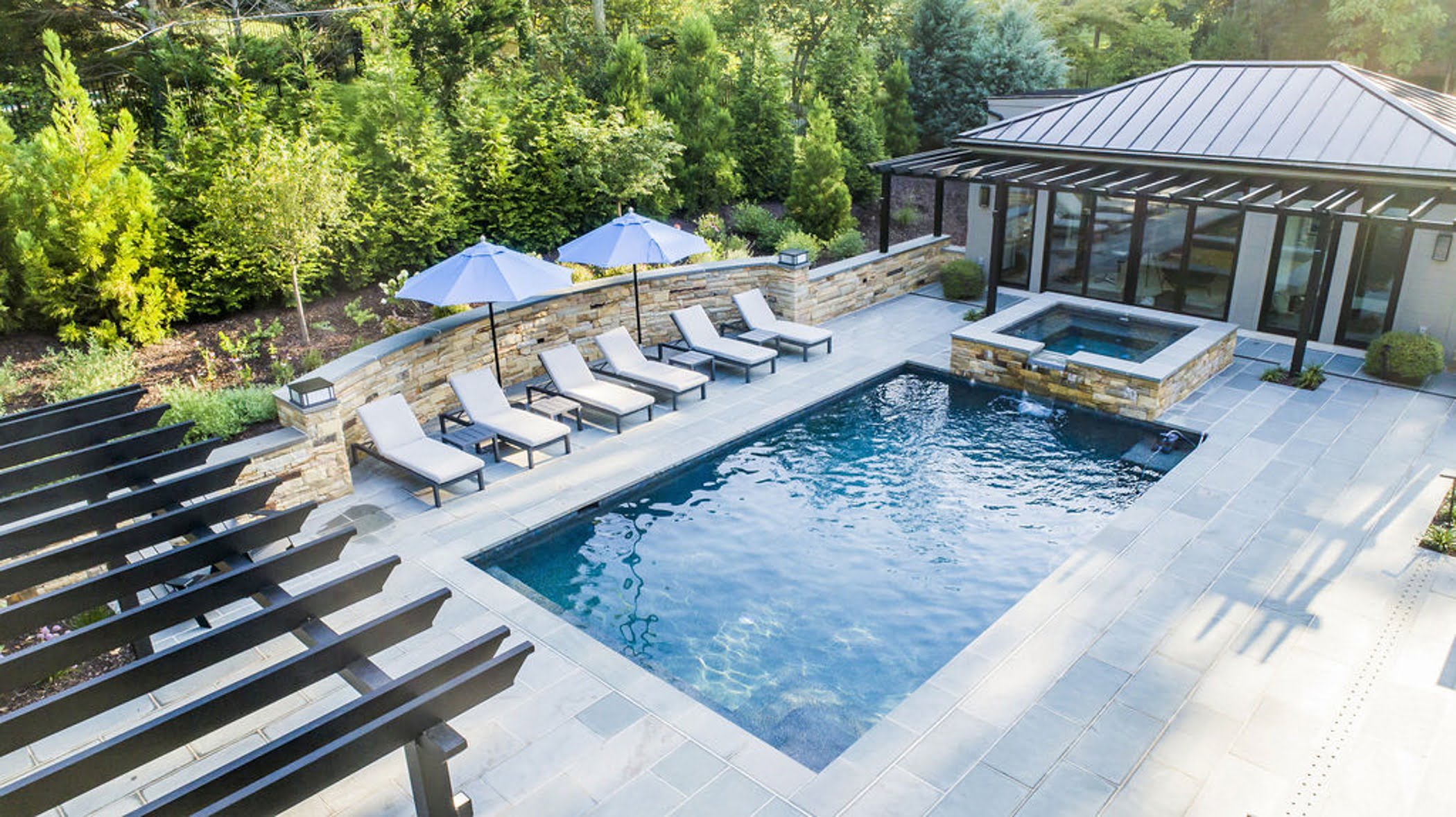 Transitional backyard patio bar and pool house with concrete pavers and cobblestone accented retaining walls and hot tub (Aerial)