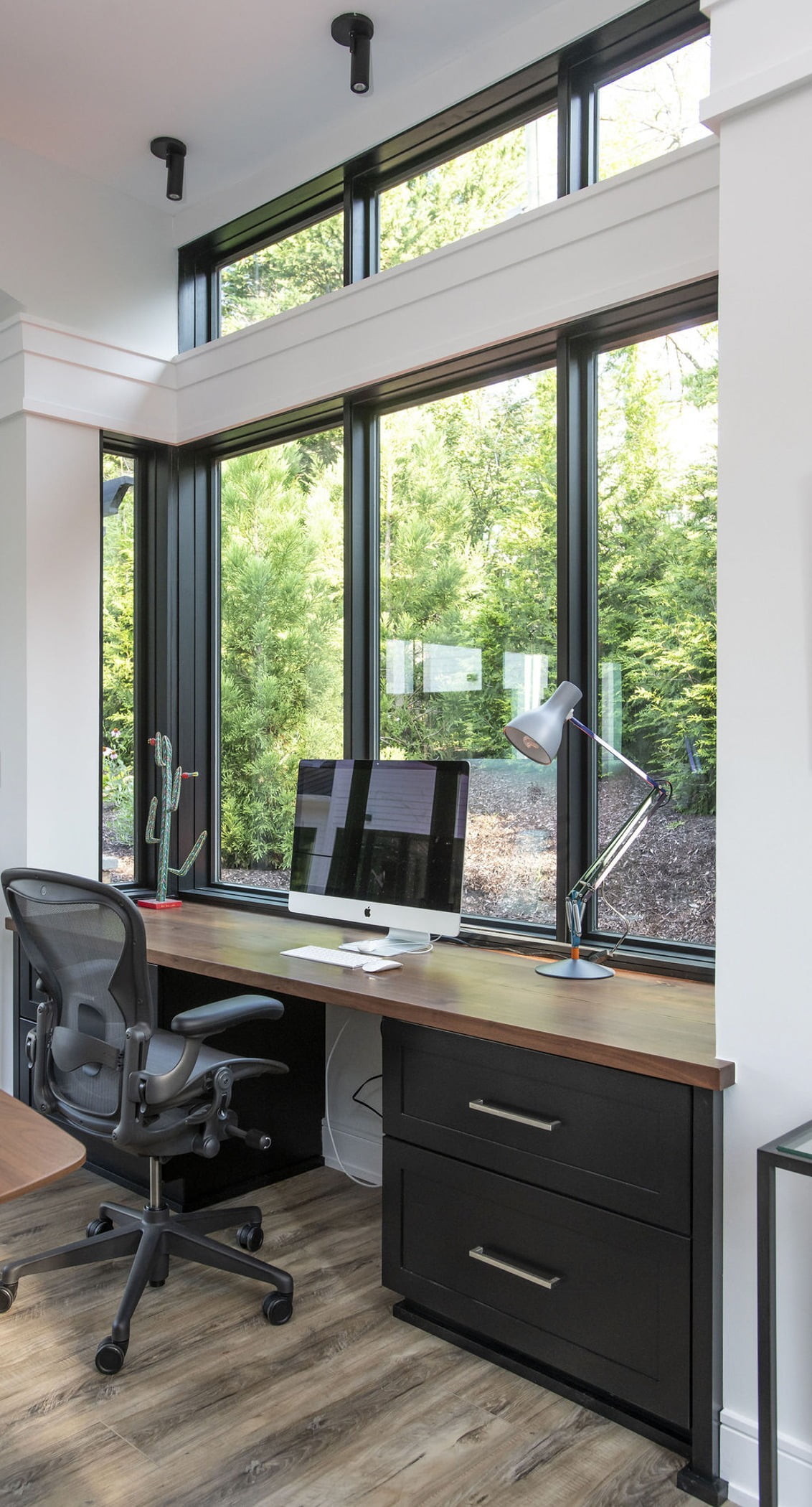 Modern office desk space with light hardwood flooring, black cabinetry, wood countertops and ceiling-high windows