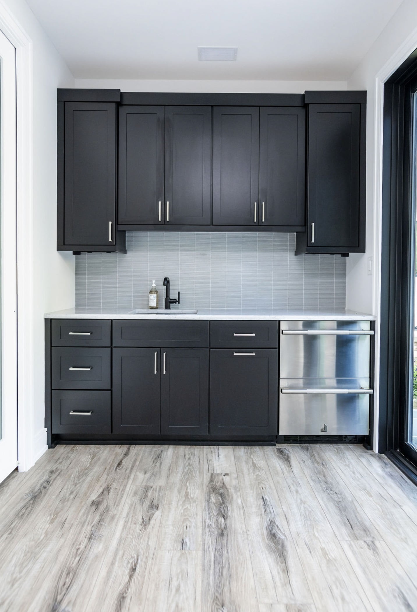 Transitional/Modern kitchenette with dark wood cabinetry, light grey tile backsplash, and light hardwood flooring