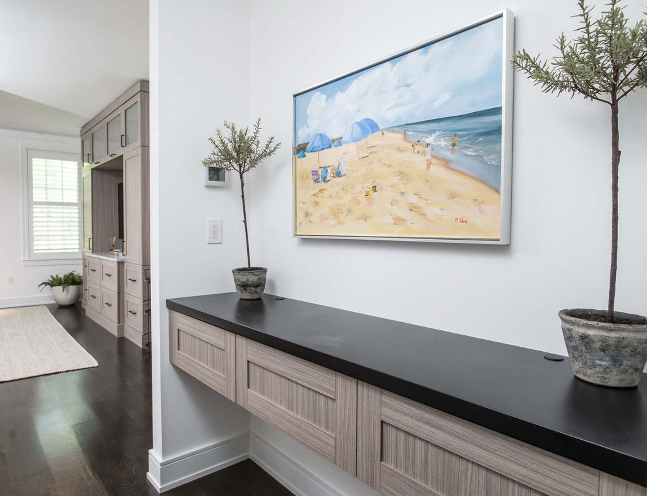 Modern bedroom design with light wood cabinetry and media center, dark wood floors and a sleek black countertop.