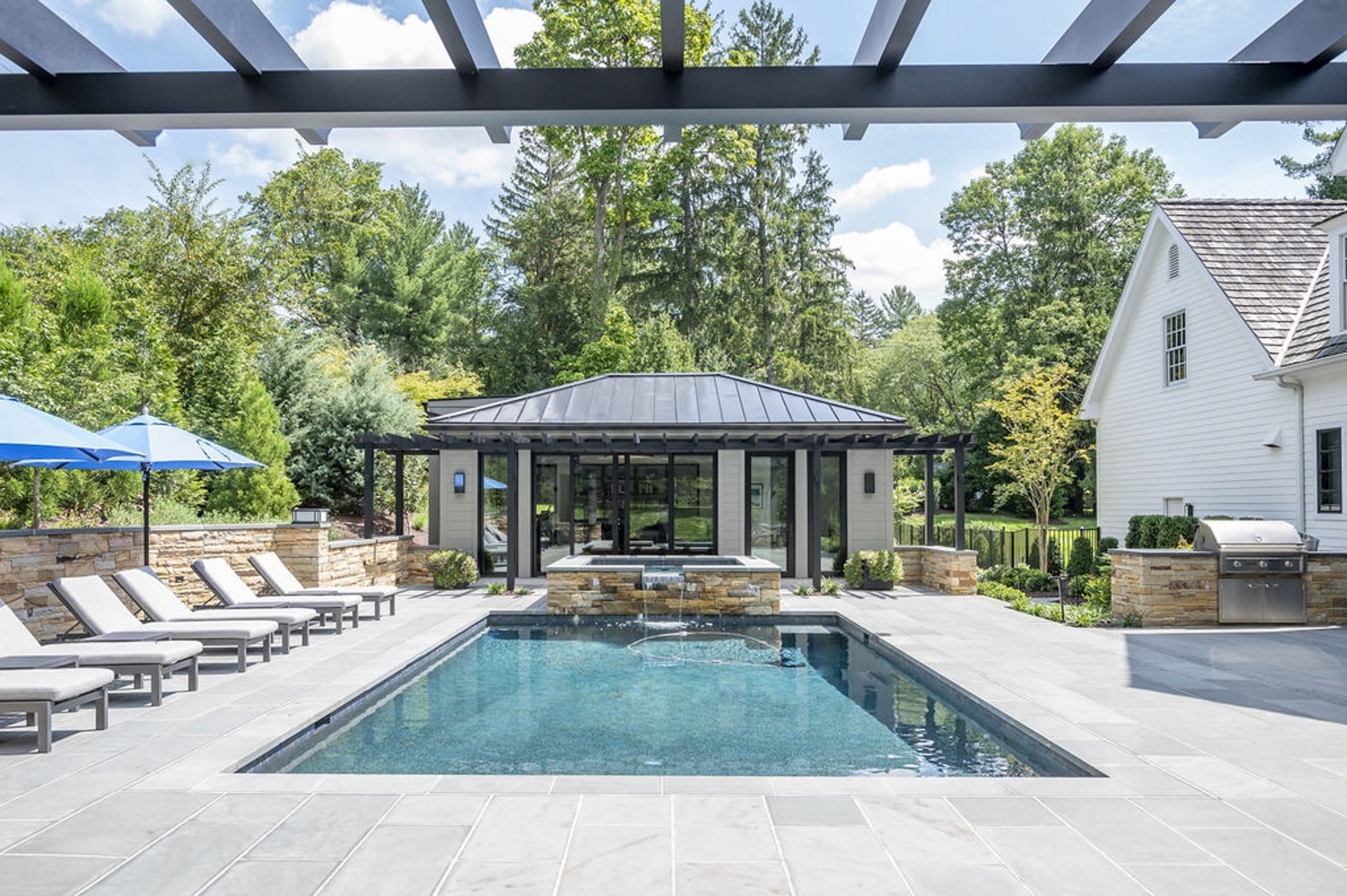 Transitional backyard patio and poolhouse with concrete pavers and cobblestone accented retaining walls and hot tub