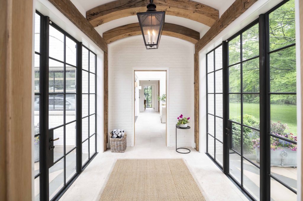 Contemporary/modern hallway with thick wooden ceiling arches, white tile flooring, and black steel framed doors and windows on either side